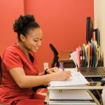 A woman in red scrubs with her hair back in a bun performs work in the lab.