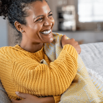 a woman holds her shoulder and waist to gather warmth from her blanket and sweater