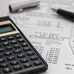 Image of a simple square calculator on the left, over a sheet of paper displaying a table of insurance expenses with a pen and cap laying across the sheet of paper