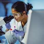 female scientist with microscope studying the four stages of cancer