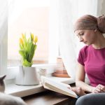 woman coping with cancer reading a book by a window